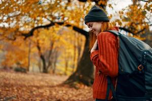 Porträt von ein Frau im ein Sweatshirt Hut mit ein Rucksack auf ihr zurück in der Nähe von das Bäume im Herbst im das Wald foto