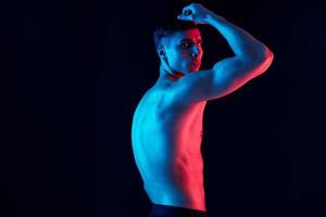 sportlich Kerl mit ein aufgepumpt Torso gebogen Über zu das Seite Fitness Modell- Neon- Licht foto