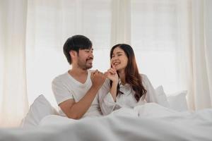 glücklich jung asiatisch Paar umarmen, neckisch, spielen fröhlich im Bett beim heim, romantisch Zeit zu verbessern Familie Verbindung. Familie Konzept. foto