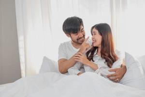 glücklich jung asiatisch Paar umarmen, neckisch, spielen fröhlich im Bett beim heim, romantisch Zeit zu verbessern Familie Verbindung. Familie Konzept. foto