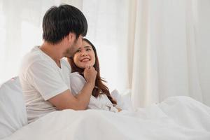 glücklich jung asiatisch Paar umarmen, neckisch, spielen fröhlich im Bett beim heim, romantisch Zeit zu verbessern Familie Verbindung. Familie Konzept. foto