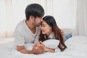 glücklich jung asiatisch Paar umarmen, neckisch, spielen fröhlich im Bett beim heim, romantisch Zeit zu verbessern Familie Verbindung. Familie Konzept. foto