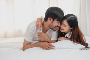 glücklich jung asiatisch Paar umarmen, neckisch, spielen fröhlich im Bett beim heim, romantisch Zeit zu verbessern Familie Verbindung. Familie Konzept. foto