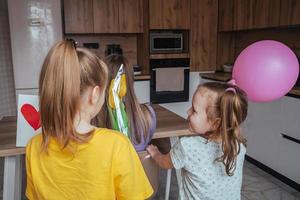 Töchter gratulieren ihr Mama auf Mutter Tag, ein Karte mit ein Herz, Blumen und ein Ballon beim Zuhause im das Küche. Kinder Überraschung ihr Mutter zum das Urlaub. foto