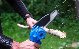 Handheld tragbar Camping elektrisch sah auf ein Batterie zum Schneiden Brennholz und Holz. Nahaufnahme, ein Hand Sägen ein Protokoll, Splitter fliegend foto