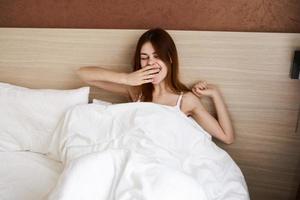Frau im Bett unter das Abdeckungen wachte auf oben im das früh Morgen abgeschnitten Aussicht von Modell- foto