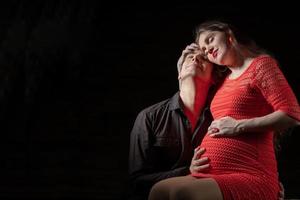 gut aussehend Mann Umarmungen ein schön schwanger Ehefrau auf ein dunkel Hintergrund. foto