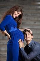 gut aussehend Mann hört zu zu Bauch von seine schön schwanger Ehefrau und lächelt foto
