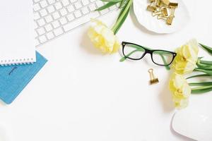 Zuhause Büro Zwischenablage Schreibtisch mit Kopieren Raum, Zwischenablage, Stift, Gläser, Notizblock und Papier Clips und Tulpe Blumen auf ein Weiß Hintergrund. eben Layout, Arbeitsplatz Layout, oben Sicht. foto