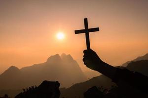 Silhouette aus Händen, die Holzkreuz auf Sonnenaufgangshintergrund, Kruzifix, Symbol des Glaubens halten. foto