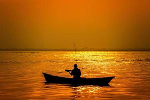 Abend golden Sonnenuntergang Zeit, ein Fischer Angeln auf das Strand auf ein Boot. foto