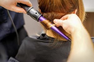 schließen oben von Haar-Stylisten Hände mit ein Eisstockschießen Eisen zum Haar Locken im ein Schönheit Salon. foto