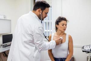 Pflege Arzt halt Stethoskop Hör mal zu zu geduldig Herz Truhe im Krankenhaus. jung Frau tun Untersuchung Untersuchung im Klinik. Gesundheitswesen Konzept. foto