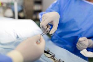 Schuss im OP-Saal, Assistent übergibt Instrumente an Chirurgen während der Operation. Chirurgen führen eine Operation durch. Professionelle Ärzte, die Operationen durchführen. foto