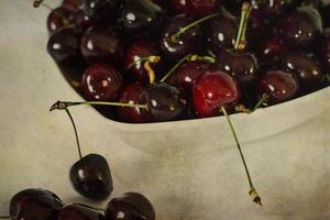 l saftig frisch Sommer- Kirschen im ein Weiß Schüssel auf ein weinlese Hintergrund foto