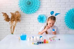 wenig Mädchen Gemälde Eier mit Blau malen. glücklich Ostern. Kind Herstellung Ostern Dekoration beim heim. foto