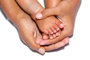 das Sanft Beine von ein Baby platziert auf das Palme von das Mutter zwei Hände auf ein Weiß Hintergrund. foto