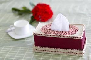 tief rot handgemacht Ballaststoff Serviette Box auf das Essen Tabelle mit ein rot Blume und ein Weiß Teetasse. Gewebe Papier Box auf Restaurant. foto