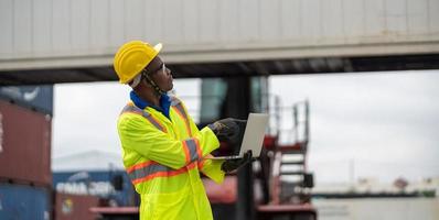 afrikanisch Techniker Dock Arbeiter im schützend Sicherheit Overall Uniform und mit Helm und verwenden Digital Tablette beim Ladung Container Versand Lagerhaus. Transport Import Export logistisch industriell foto