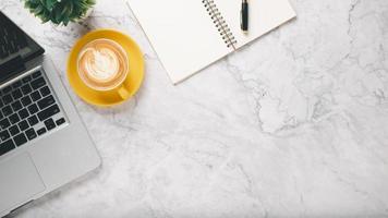 Weiß Büro Schreibtisch Arbeitsplatz mit Laptop Computer, Stift, Notizbuch und Tasse von Kaffee, oben Aussicht eben legen mit Kopieren Raum. foto