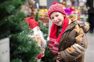 froh Kind mit ein Spielzeug Santa claus beim das Weihnachten Markt. glücklich wenig Junge beim Weihnachten. foto