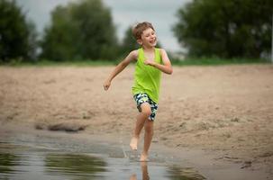 glücklich Junge läuft entlang das Strand. ein Kind Theaterstücke durch das Fluss. foto