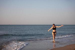 ein mittleren Alters Frau Spaziergänge entlang das Strand im ein Badeanzug. foto