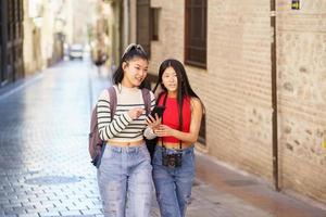 asiatisch weiblich Touristen Gehen auf Stadt Straße mit Smartphone foto