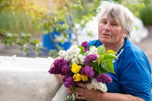 grau haarig Alten Frau mit ein Strauß von Flieder draußen. Rentner im das Land. foto