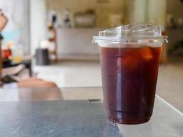 vereist schwarz Kaffee Americano im ein groß Becher einstellen auf ein gespiegelt hölzern Tabelle im das Cafe. erfrischend trinken und aufwachen oben im das Morgen von das Tag foto