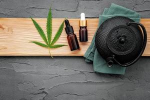 Weinlese-Teekanne mit Cannabis-Kräutertee und frischen Marihuana-Blättern, die auf Betonhintergrund aufgestellt werden foto