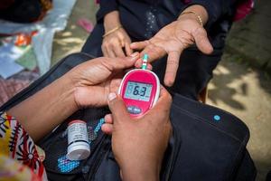 Frau Überprüfung Zucker Niveau mit Glukometer mit ein Blut Stichprobe beim Narsingdi, Bangladesch. lernen zu verwenden ein Blutzuckermessgerät. Konzept von Diabetes Behandlung. foto