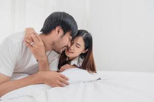 glücklich jung asiatisch Paar umarmen, neckisch, spielen fröhlich im Bett beim heim, romantisch Zeit zu verbessern Familie Verbindung. Familie Konzept. foto