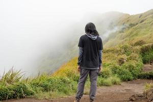 Mann Wandern zu das oben Berg, mit Savana Spur und wolkig Schwingungen. das Foto ist geeignet zu verwenden zum Abenteuer Inhalt Medien, Natur Poster und Wald Hintergrund.