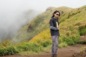 Mann Wandern zu das oben Berg, mit Savana Spur und wolkig Schwingungen. das Foto ist geeignet zu verwenden zum Abenteuer Inhalt Medien, Natur Poster und Wald Hintergrund.