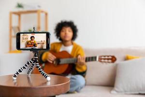 Blogger Gitarrist. afrikanisch amerikanisch Mädchen Blogger spielen Gitarre reden zu Webcam Aufzeichnung vlog. Sozial Medien Influencer Frau Streaming beim Zuhause drinnen. Musik- Inhalt Schöpfer Übertragung Lernprogramm. foto