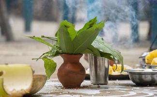 Hindu Kultur Anbetung Elemente Nahansicht mit ein Lehm Topf, Grün Blätter, Stahl Glas, und Teller. traditionell Hindu Hochzeit und Puja Elemente mit ein rauchig Hintergrund. dekoriert Hindu Gelegenheiten. foto