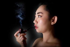 Frau, die einen Pfeifentabak auf schwarzem Hintergrund raucht foto