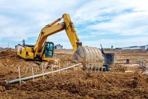 Bagger graben die Gräben auf einer Baustelle. Graben zum Verlegen von externen Abwasserrohren. Abwasserentsorgungssystem für ein mehrstöckiges Gebäude. Graben des Grubenfundaments foto