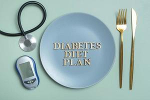 Diabetes Diät planen Text. Stethoskop, Glukometer und Teller mit Besteck auf farbig Hintergrund eben legen, oben Aussicht foto