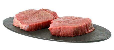 zwei runden roh Rindfleisch Steak auf ein schwarz Oval Schneiden Planke, Weiß isoliert Hintergrund foto