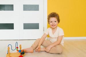 vierjährig Junge sitzt auf das Fußboden und Theaterstücke mit Spielzeuge beim Zuhause oder im Kindergarten foto