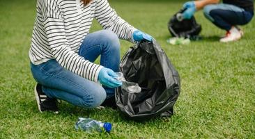 zwei personen, die müllplastikflasche in einer schwarzen tasche im park halten. reinigung, verschmutzung, ökologie und plastikkonzept. foto