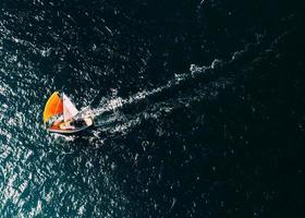 Antenne Drohne oben Nieder Foto von ein Segelboot mit ein hell Orange Mast gegen ein tief Blau Ozean