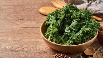 Konzept von frisch Grünkohl Blätter Salat im ein Schüssel auf hölzern Tabelle Hintergrund. Grün Grünkohl Blätter Salat Essen im das Küche. Löffel, Gabel foto