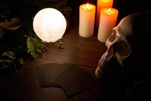 Wahrsagen auf ein hölzern Tabelle und ein Weiß Kerze mit ein Kristall Ball und Karten auf dunkel Hintergrund. vorhersagen, Vorhersage, Horoskop, makaber, Hexerei, Schädel foto