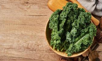 Konzept von frisch Grünkohl Blätter Salat im ein Schüssel auf hölzern Tabelle Hintergrund. Grün Grünkohl Blätter Salat Essen im das Küche. eben legen, oben Sicht, Löffel, Gabel foto