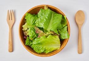 frisch Salat von Grün Blätter im ein hölzern Schüssel auf Weiß sauber Stimmung Hintergrund mit Kopieren Raum. Löffel und Gabel foto