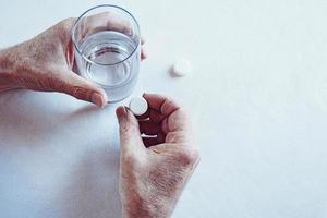 Alten Mann Hände nehmen Medizin Pille mit ein Glas von Wasser foto