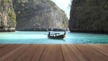 Holzplatte Tisch auf der Draufsicht auf schönes Meer und Holzboot mit Bergen im tropischen Resort während eines Sommertages